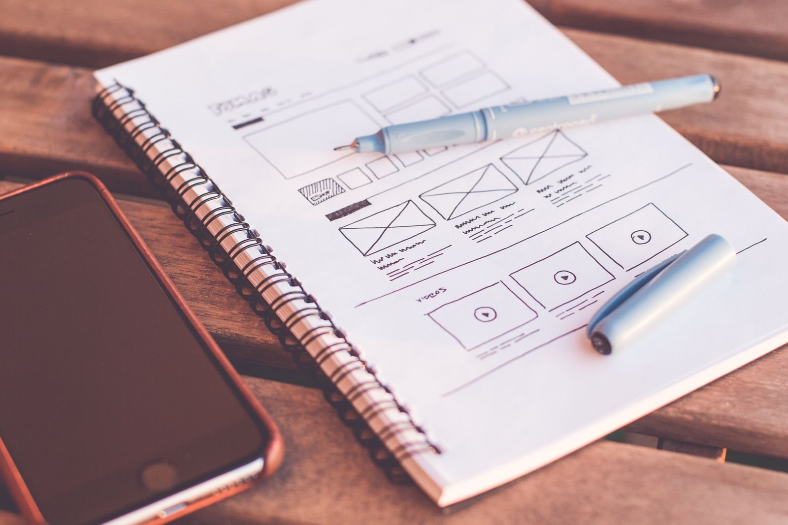 Hand-drawn app wireframes in a notebook beside a phone