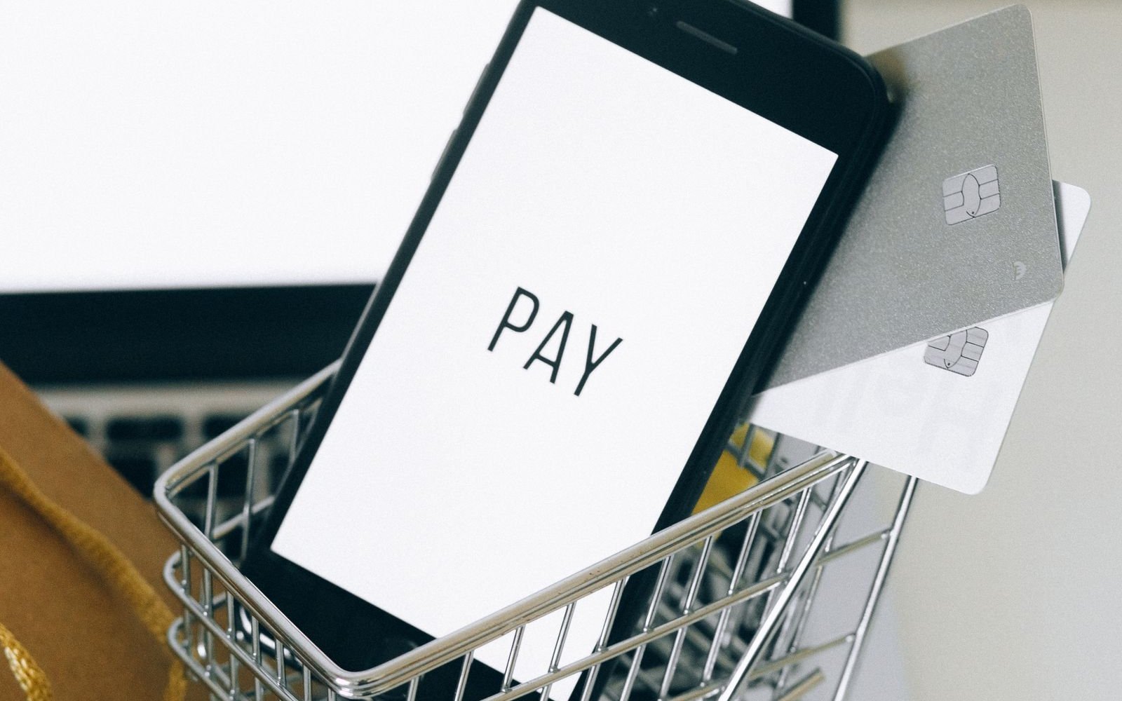 Phone showing a pay screen in a miniature shopping trolley beside bank cards