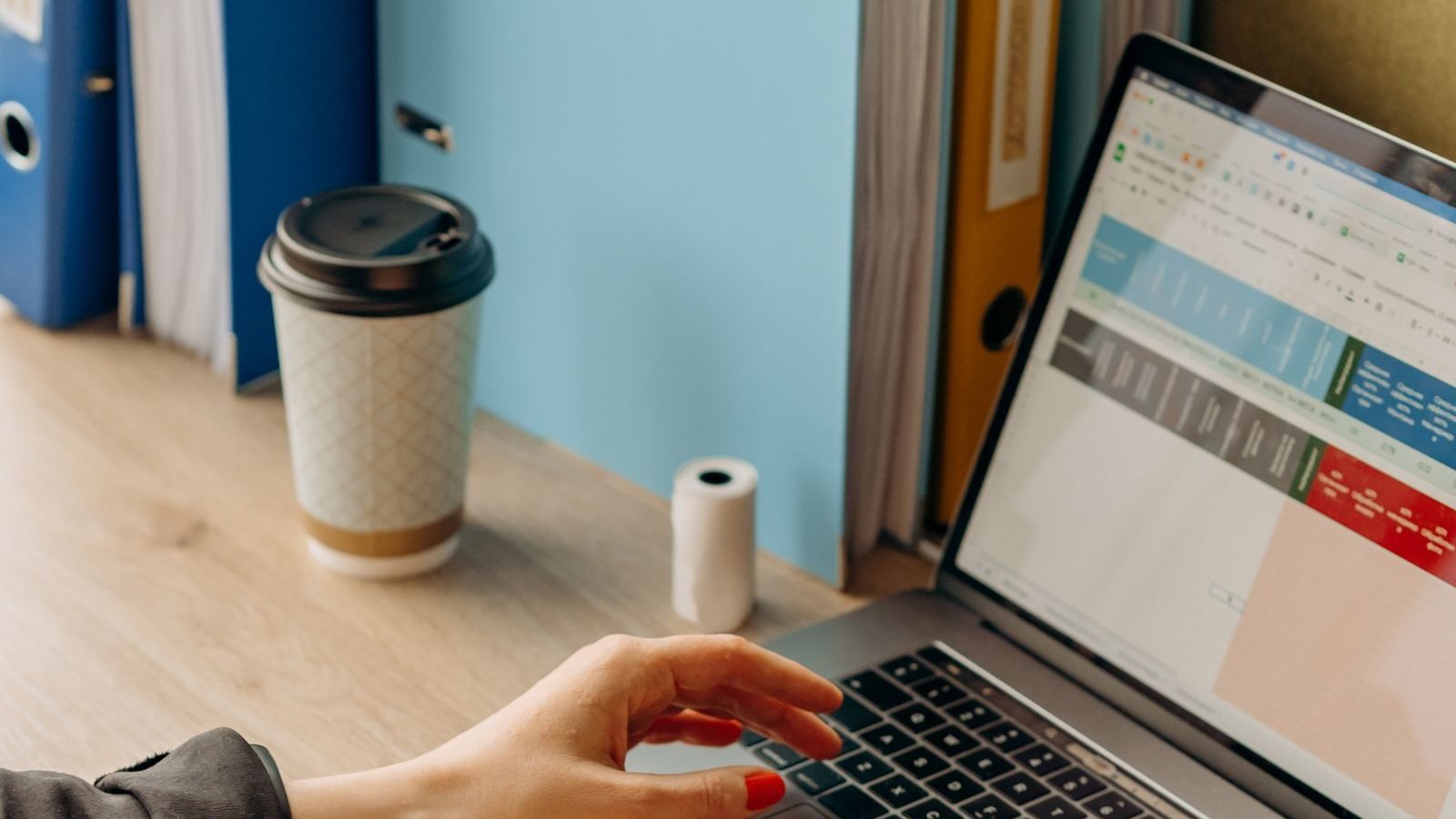 Spreadsheet open on a laptop beside office files and a coffee cup
