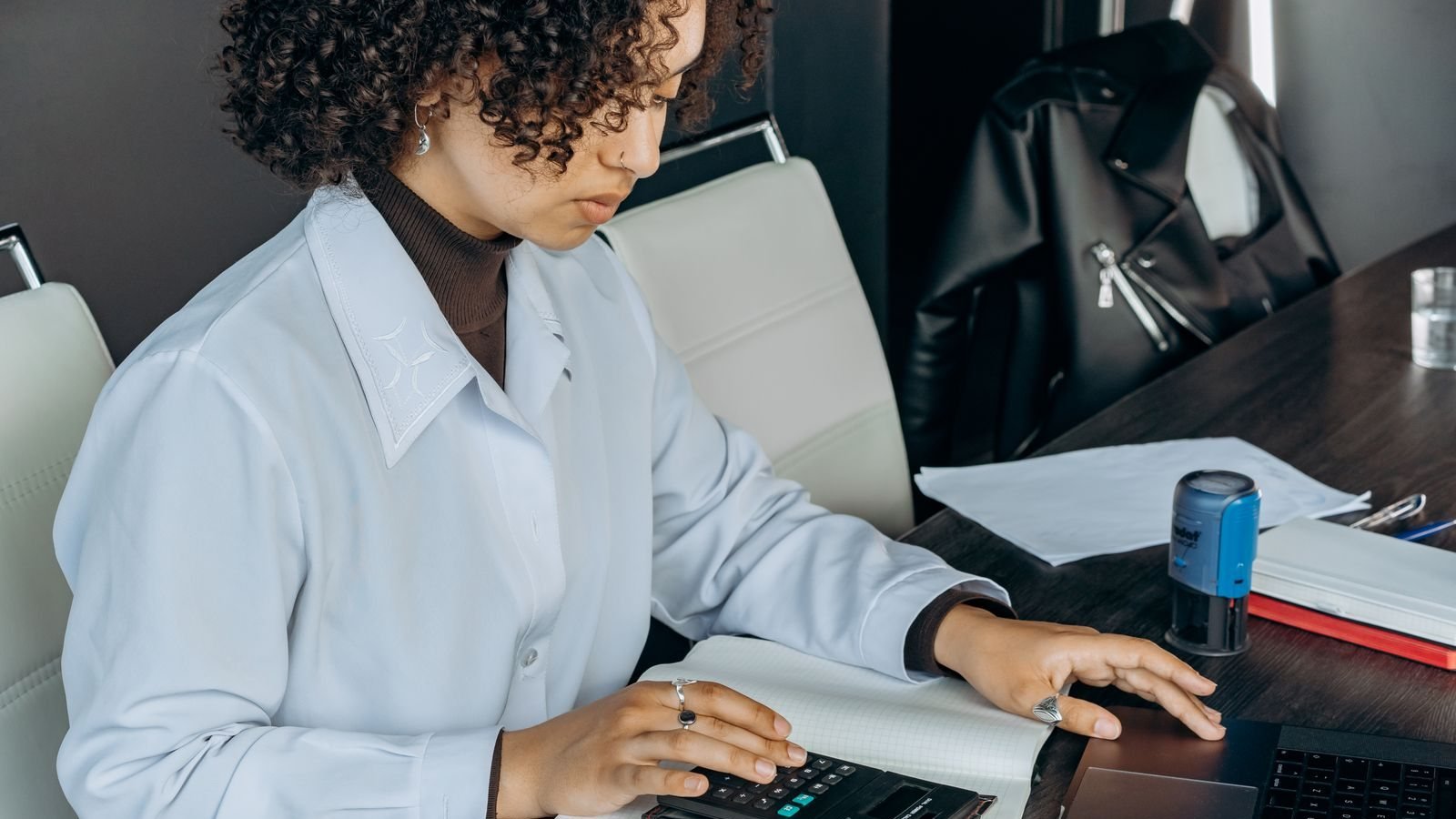Accountant working on a calculator beside a laptop and ledger